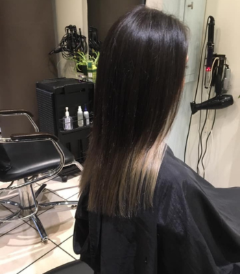 Person with long dark hair in a professional salon chair at KAST hair studio in Port Moody, showing hair styling results with salon products and equipment visible in the background