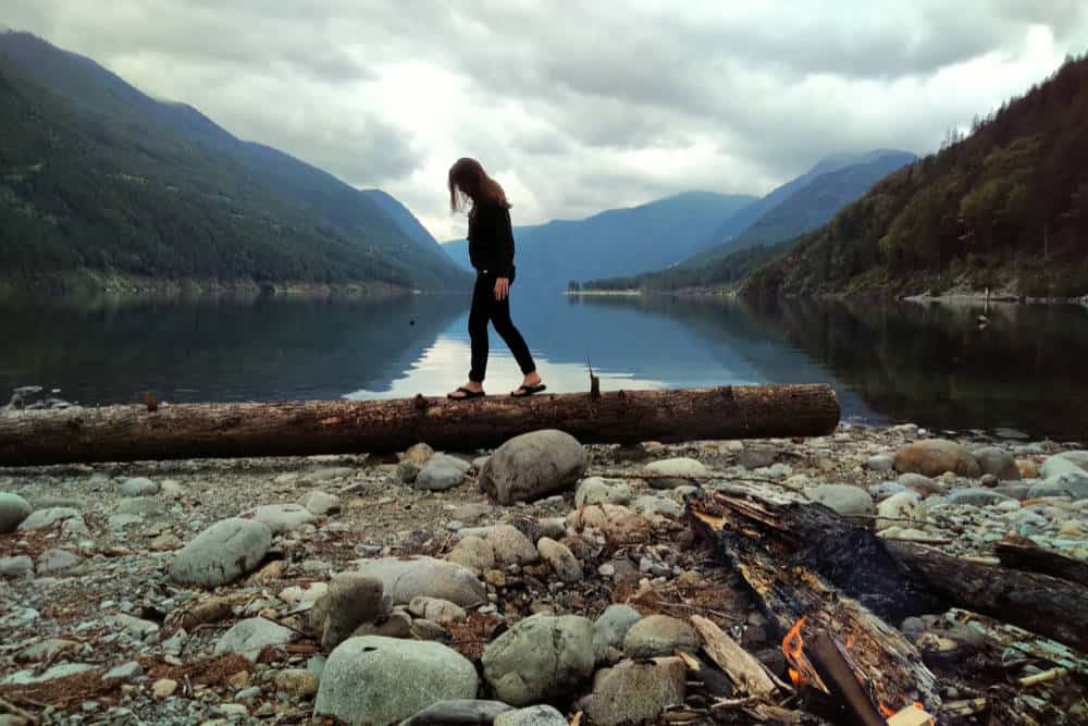 Person standing on a fallen log at a peaceful lakeside with mountains in the background near Port Moody, British Columbia