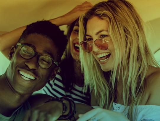 Three happy friends wearing fashionable eyeglasses smiling together indoors, showcasing modern eyewear styles available in Port Moody