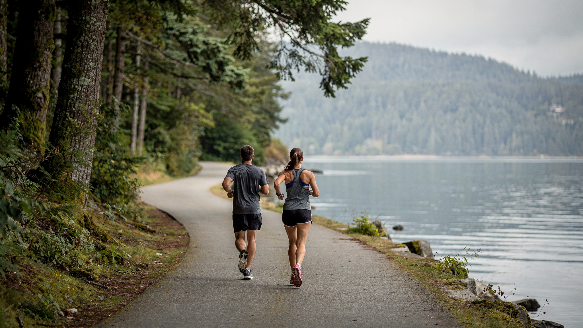 Two runners jogging along a waterfront trail beside Burrard Inlet in Port Moody