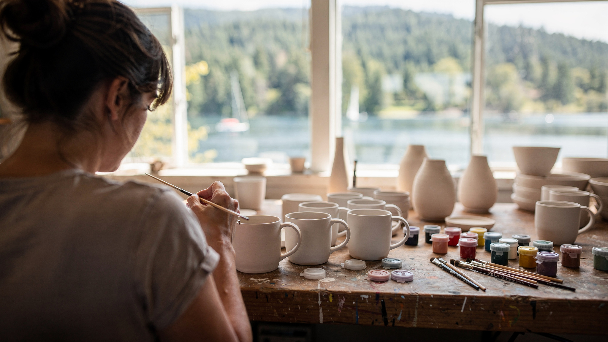 hands painting a ceramic mug at a pottery studio table overlooking the water in Port Moody