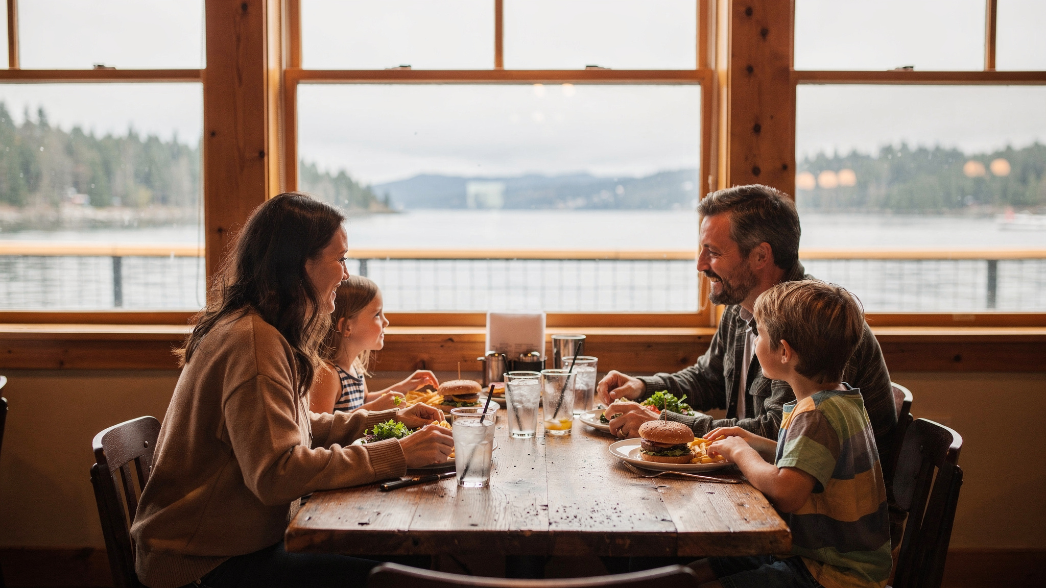 Family enjoying a meal together at a window table overlooking the water in Port Moody