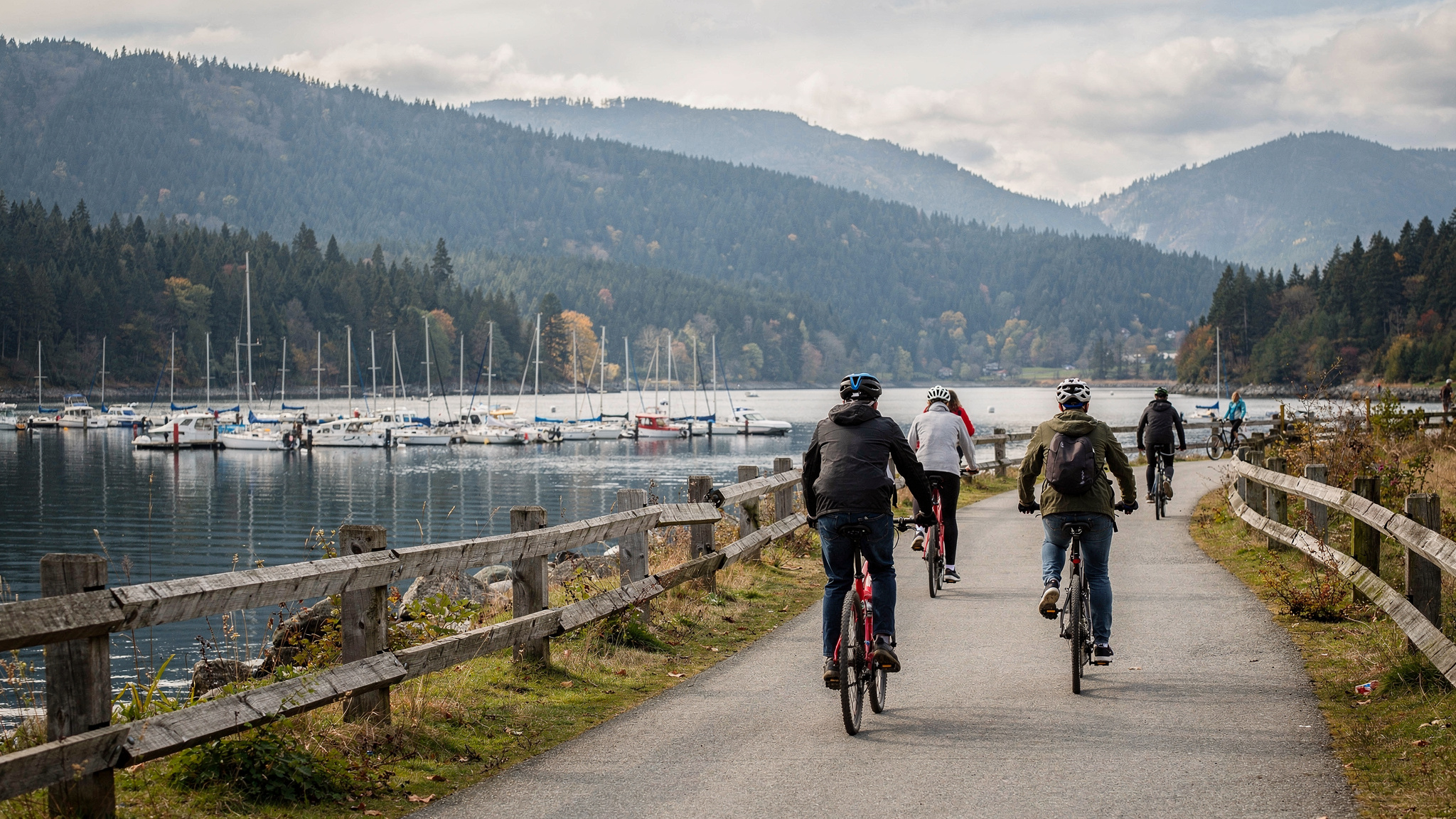 Cyclists riding the waterfront trail at Rocky Point Park in Port Moody with the marina and mountains behind them