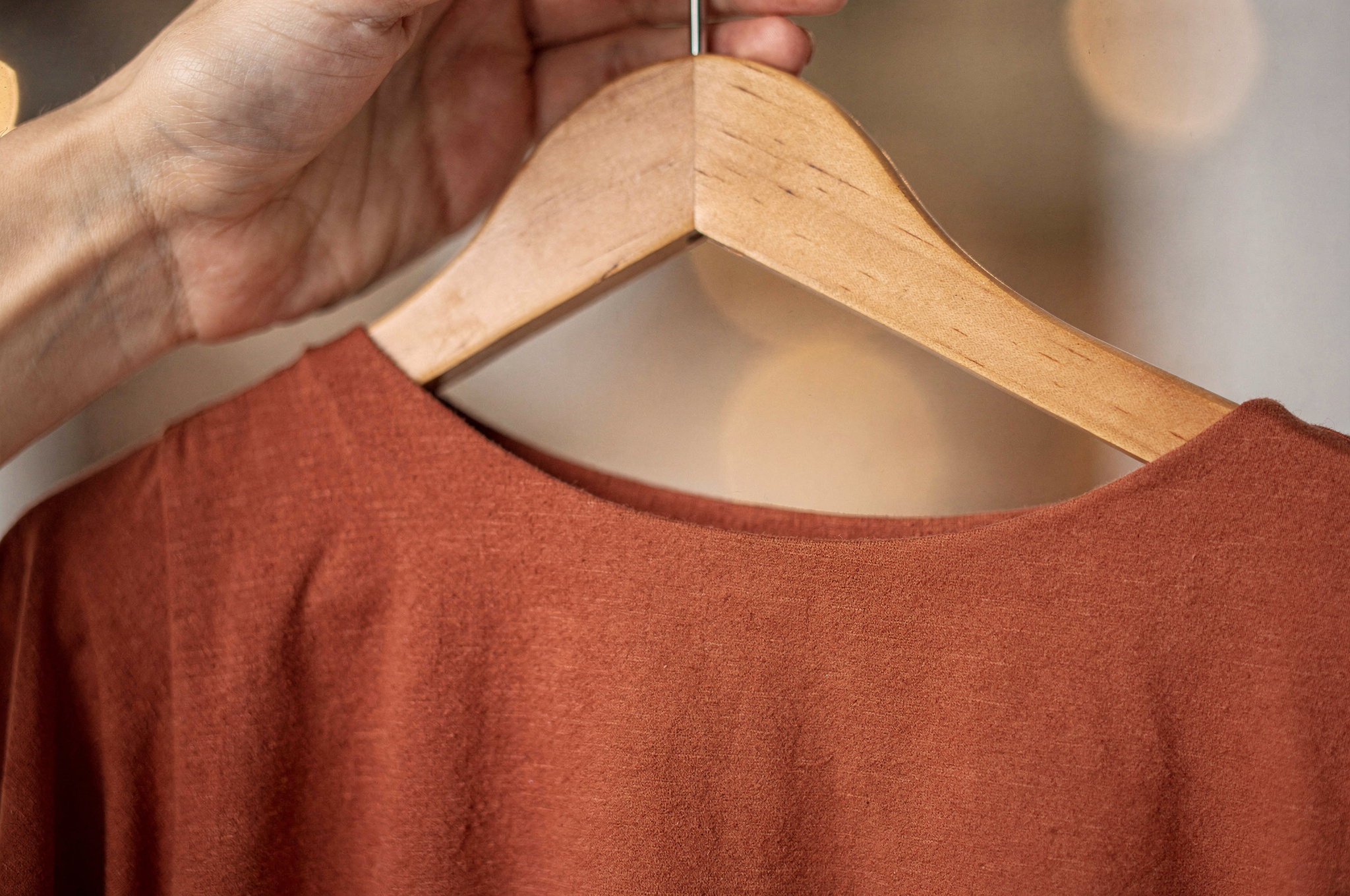 Hand holding a clothing item on a wooden hanger in a boutique
