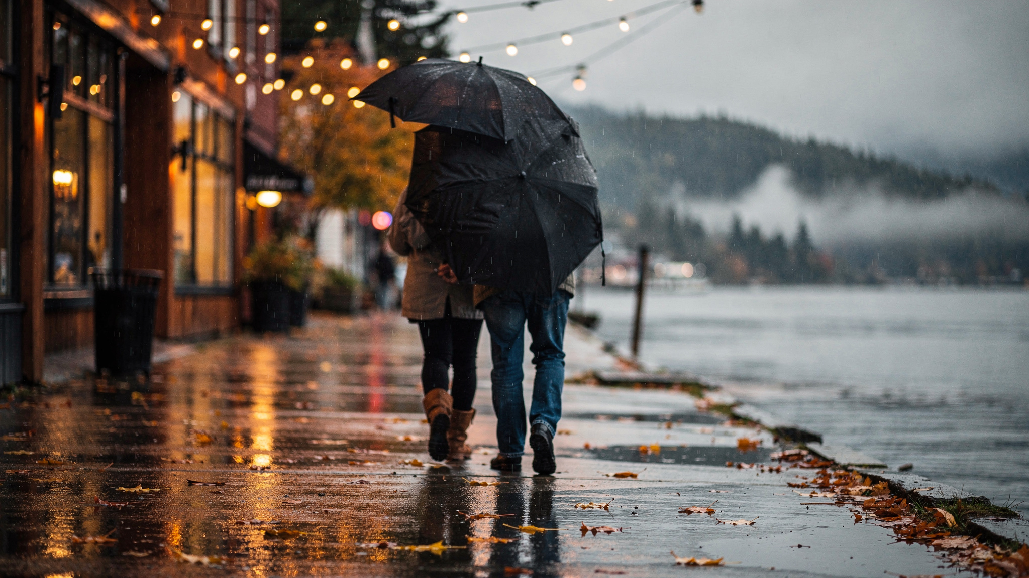 Two people walking under umbrellas along a rainy waterfront sidewalk in Port Moody, BC